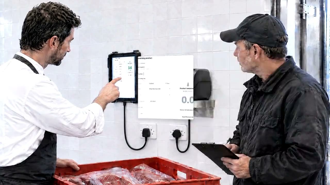A chef and a delivery driver at the wall tablet beside a crate of meat
