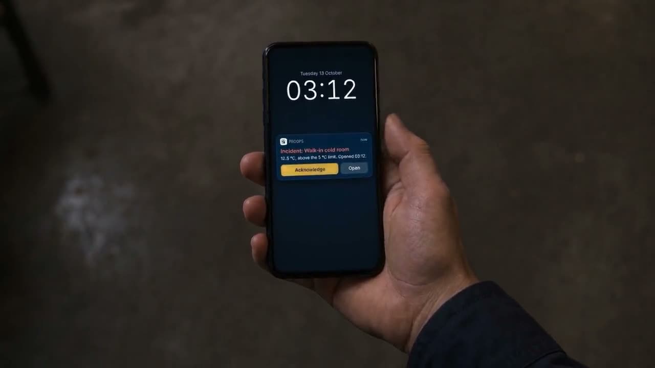 A hand holds a phone at 03:12 showing a ProOps notification